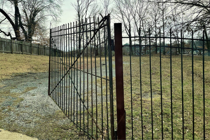 An open fence to a vacant lot on a cloudy day