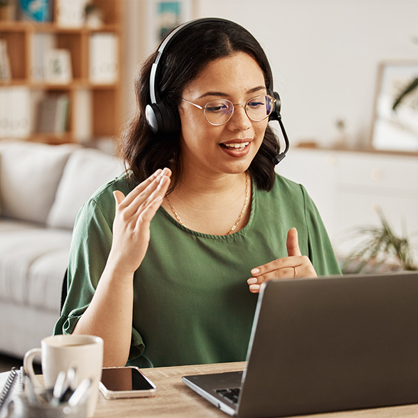 Woman on a headset speaking and looking at a laptop