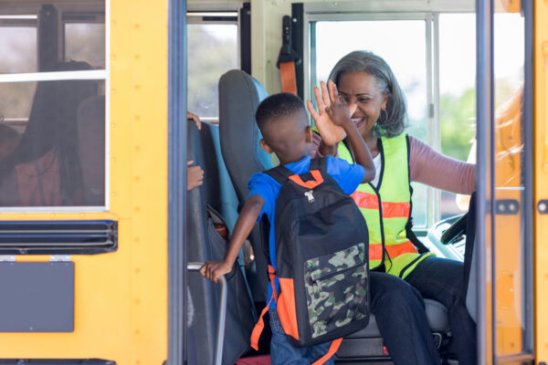 female black bus driver highfives black child as they get on the bus.