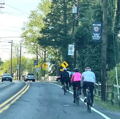 Three bicyclists on a busy road, riding close to the white line on the right