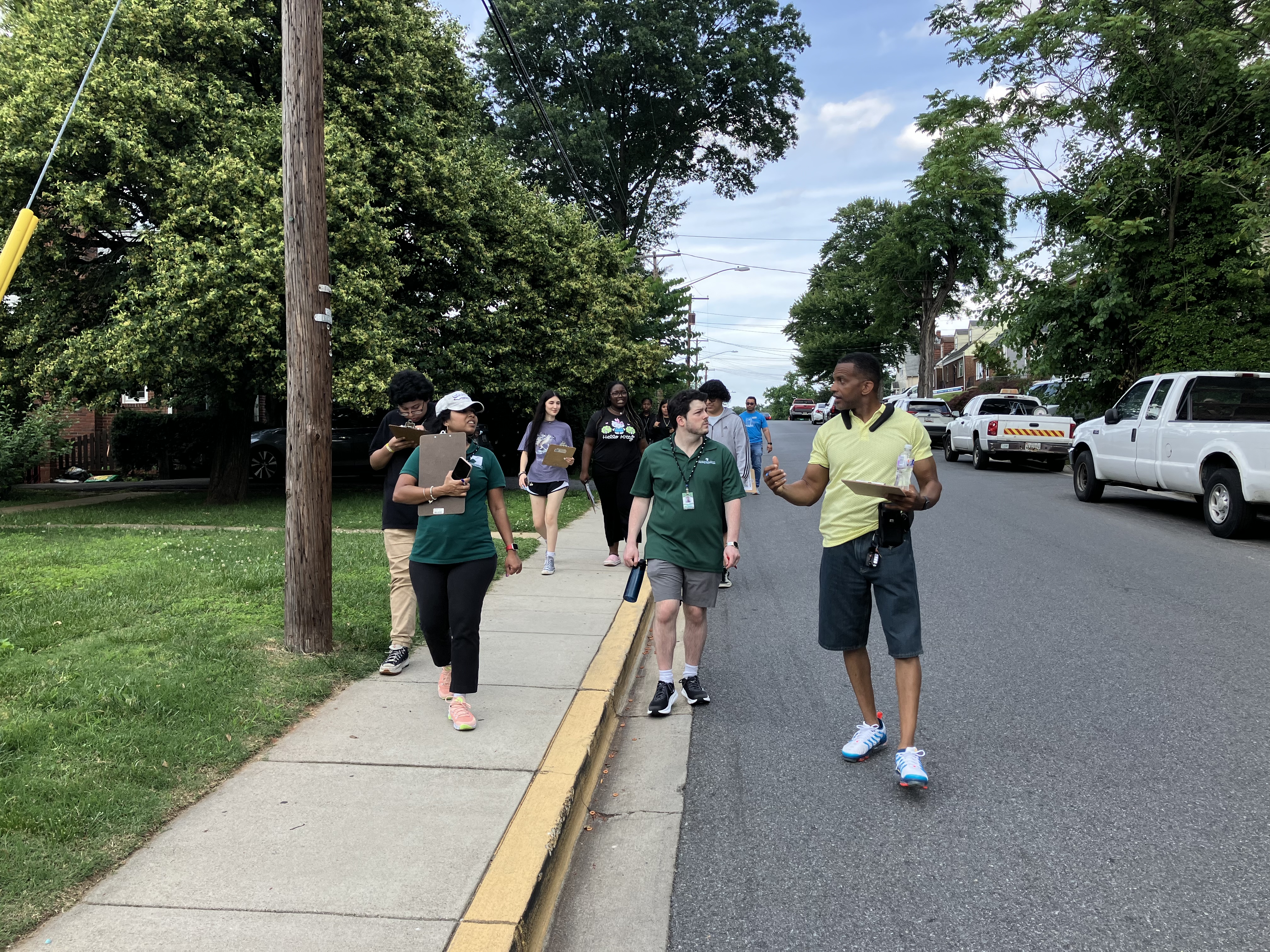 A group of people walking along a sidewalk and looking at houses in the neighborhood.