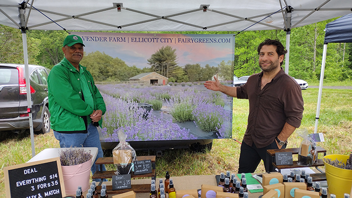 Farmers at market next to lavendar farm sign.
