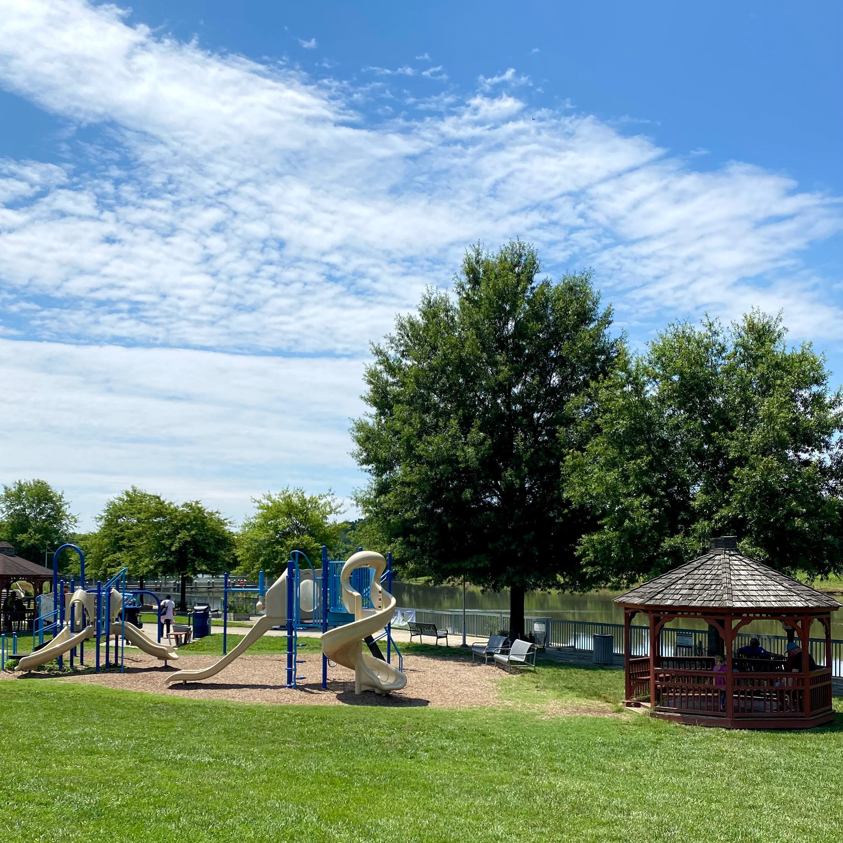 A playground with cover play house, slides, and green grass.