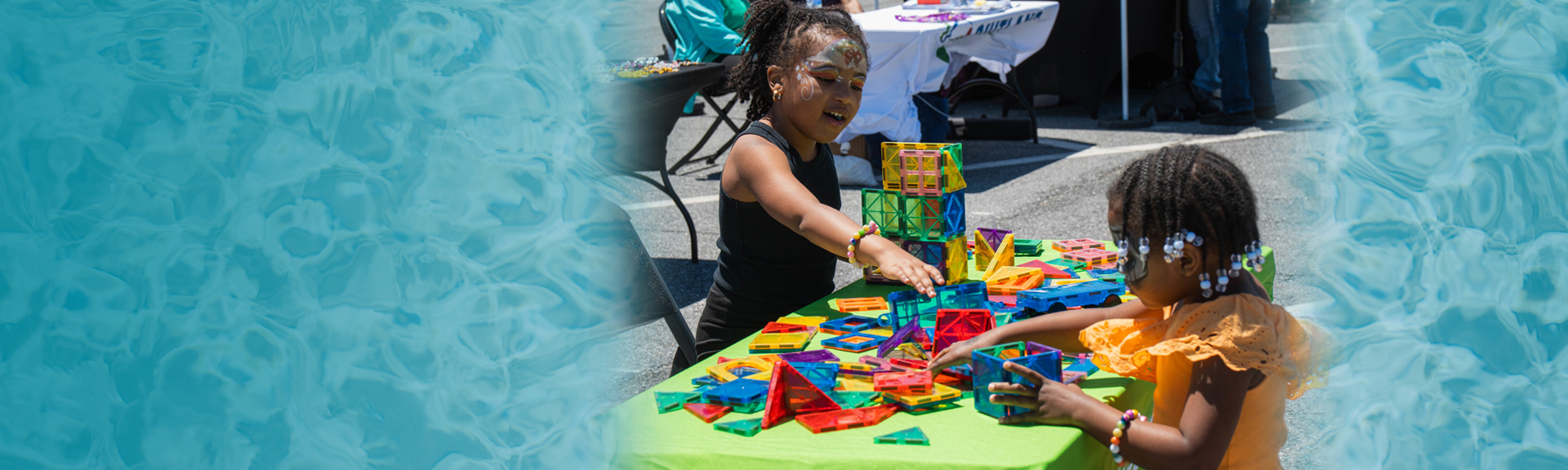Two young girls build with colorful magnetic tiles at an outdoor Suitland festival activity table.