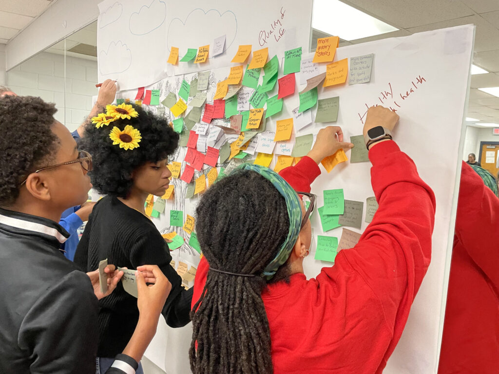 Two young women and one young man add notes to a board at a Walker Mill Community Meeting.