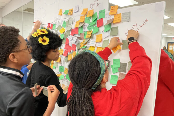 Two young women and one young man add notes to a board at a Walker Mill Community Meeting.